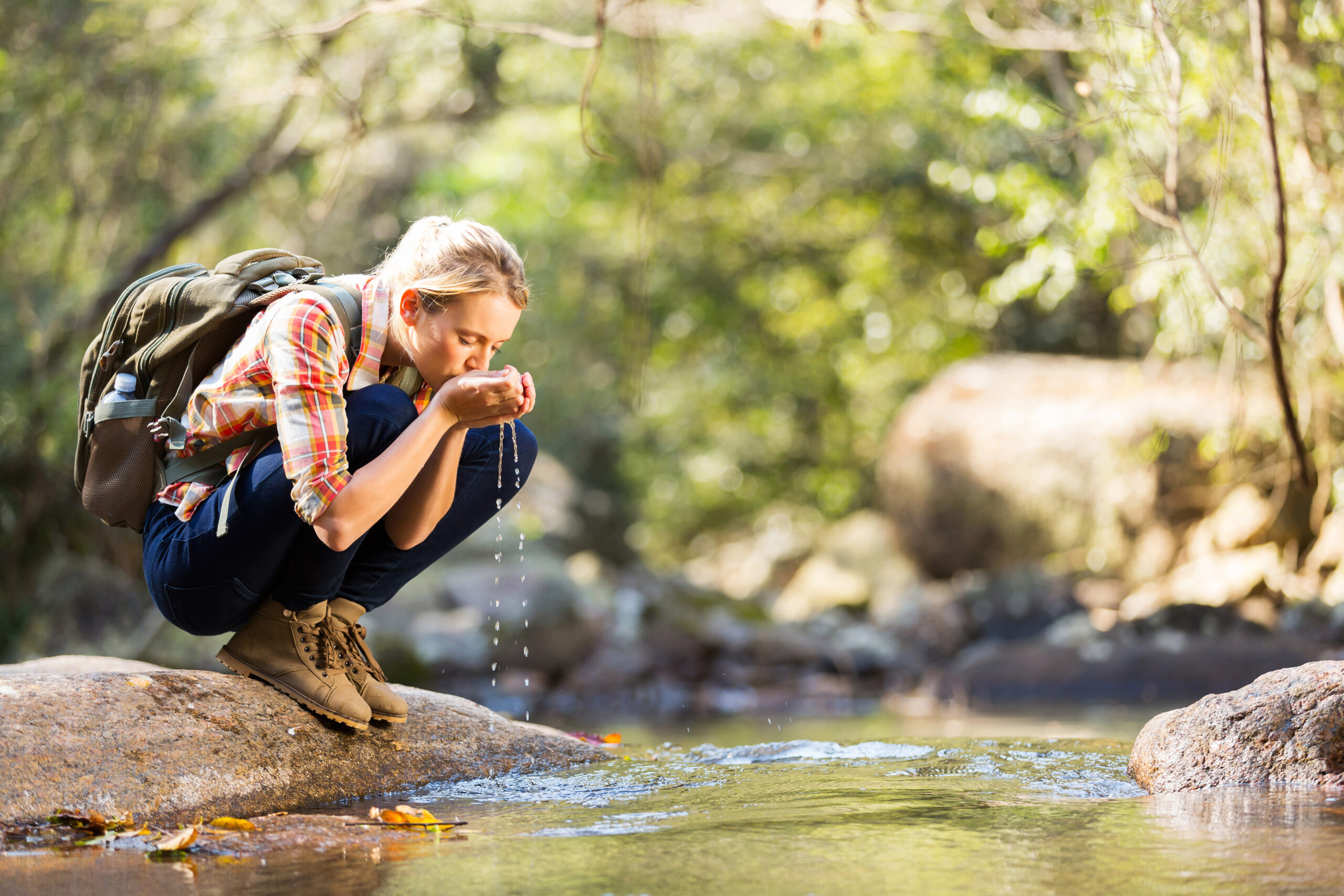 young hiker drinking stream water in mountain